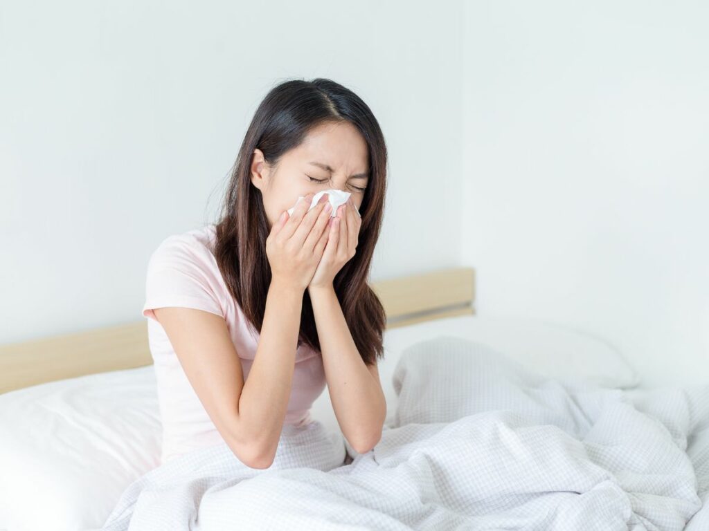 woman sneezing on bed